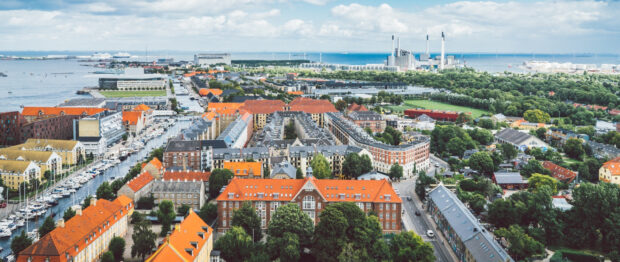 A panoramic view of Copenhagen city featuring red rooftops and a waterfront canal with boats