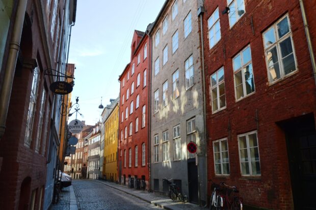 Colorful buildings line a narrow cobblestone street in Copenhagen with bicycles parked along the walls