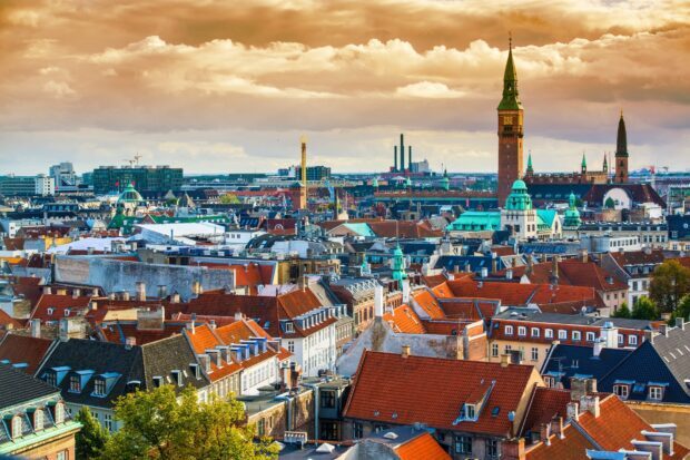 A panoramic view of Copenhagen cityscape with historic buildings and a prominent clock tower under a cloudy sky