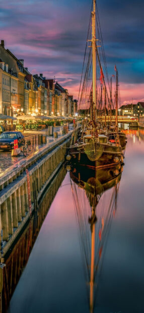A historic ship docked in Copenhagen canal at sunset with colorful buildings lining the waterfront