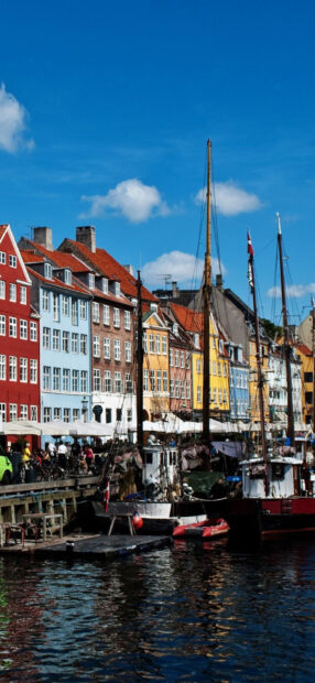 Colorful historic buildings along the Copenhagen waterfront with boats and clear blue sky