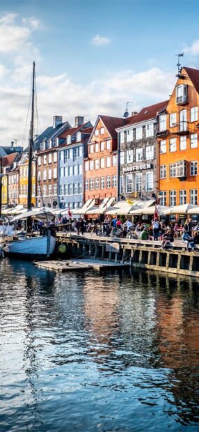 Colorful historical buildings along the waterfront in Copenhagen with people sitting and a boat docked
