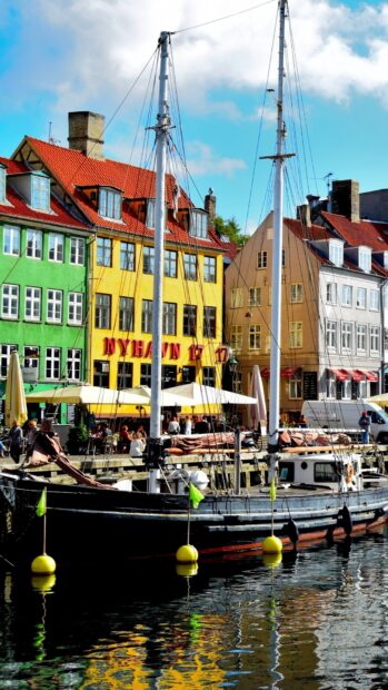 Colorful Copenhagen buildings along the waterfront with a docked sailboat in clear daylight