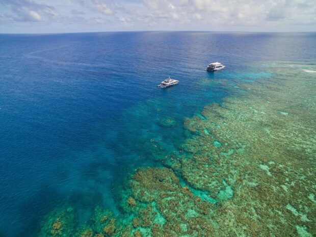 Aerial view of coral sea with boats and clear turquoise water in the coral sea