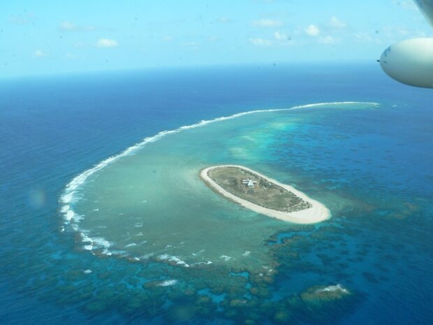 Aerial view of a coral sea island with clear turquoise water and a small structure on the shore