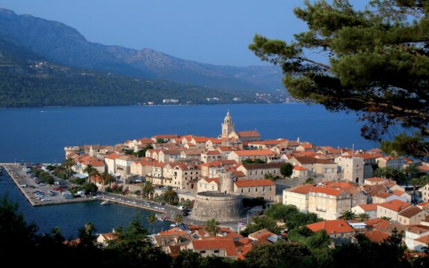 A panoramic view of a historic Croatian town with orange rooftops by the sea in a mountainous region