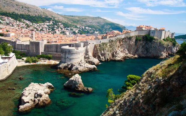 Ancient Croatian coastal fortress and town with clear blue sea and rocky cliffs viewed from hillside