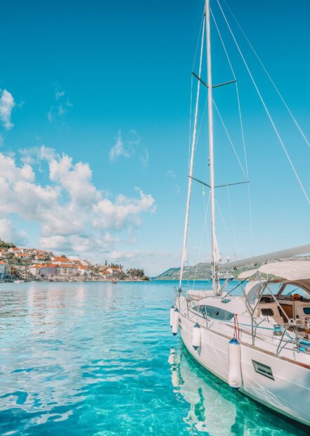 A white sailboat docked in clear turquoise water near a coastal town in Croatia