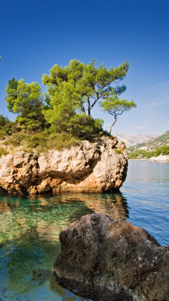 Clear waters surrounding rocky islands in Croatia with green trees and blue sky