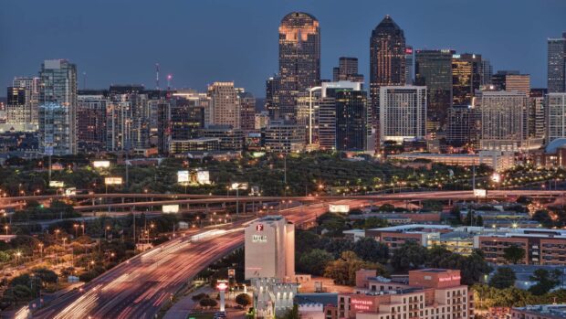 Night view of Dallas Texas city skyline with illuminated buildings and busy highway traffic