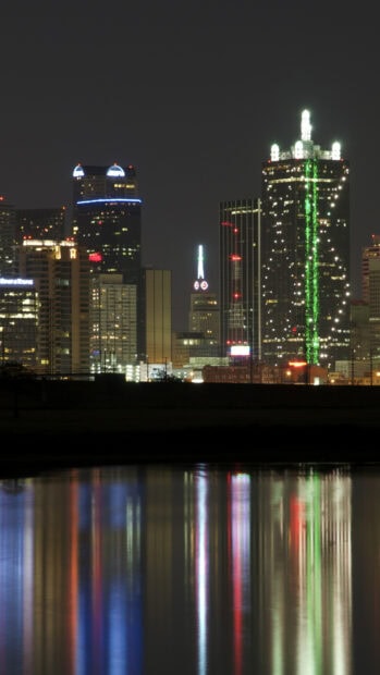 Night view of Dallas Texas cityscape with illuminated skyscrapers and colorful light reflections on water
