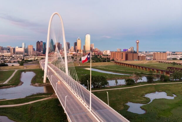 The Dallas cityscape with a bridge and Texas flag under a clear sky at sunset