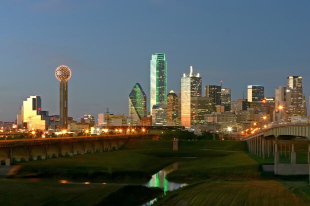 The Dallas Texas skyline with illuminated buildings and a bridge at dusk
