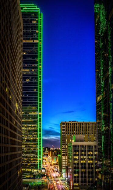 Nighttime cityscape of Dallas Texas with tall buildings and green lights lining the streets
