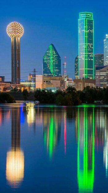 Iconic skyline in Dallas Texas with illuminated buildings reflected on calm water at dusk