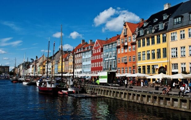 Colorful buildings lined along a canal in Denmark with boats docked under a blue sky