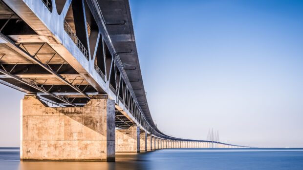 A long concrete and steel bridge extending over calm blue water in Denmark