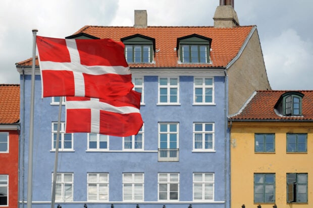 Danish flag waving in front of colorful Denmark buildings