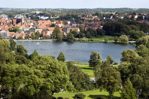 A scenic view of Denmark city with a lake and lush greenery surrounding the buildings