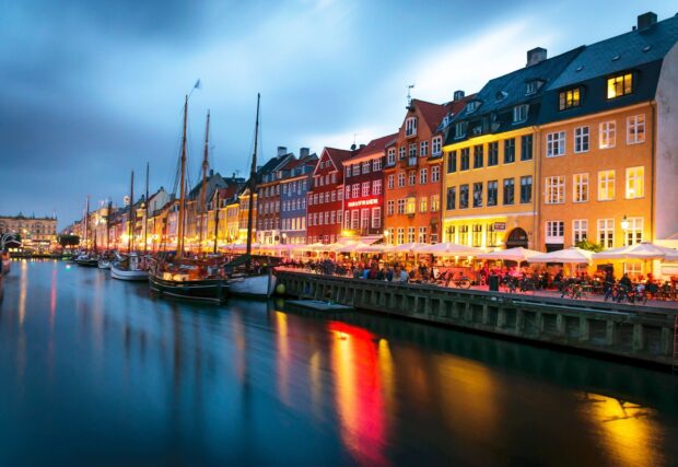 Colorful buildings along a canal in Denmark reflecting lights on the water at dusk
