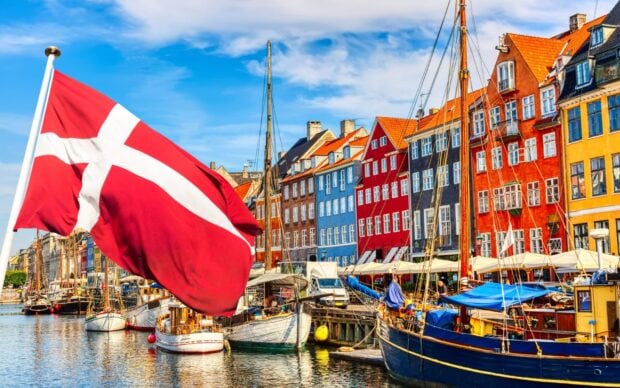 A Danish flag waving over colorful buildings and boats along a canal in Denmark