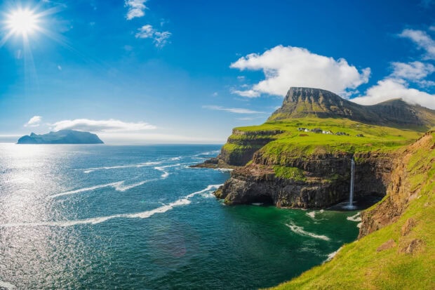 Cliffside green landscape with waterfall and Denmark coastline under blue sky