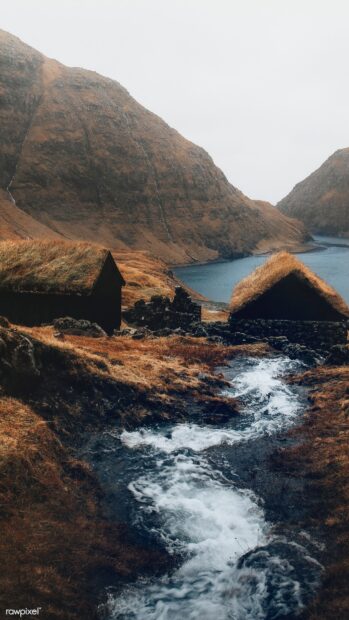 A scenic view of Denmark with traditional houses near a flowing stream and mountainous landscape