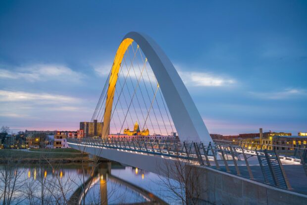 Modern Des Moines bridge with golden lights reflecting on calm river at dusk