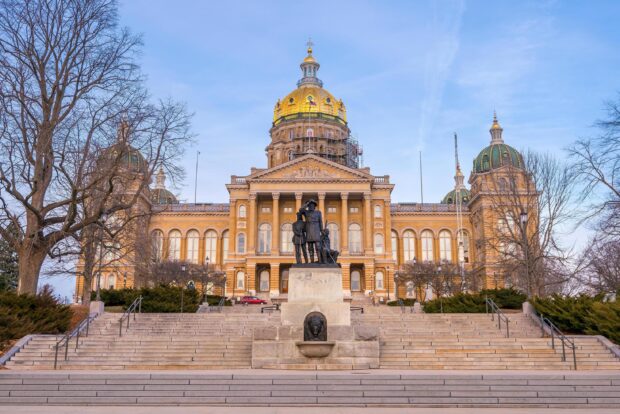 The Des Moines capitol building with golden dome and statue in front on a clear day