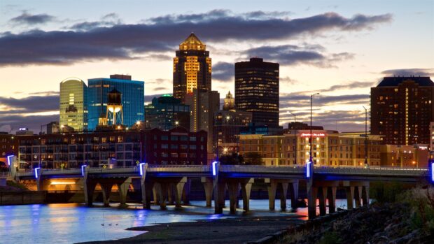 The Des Moines cityscape with illuminated buildings and a river bridge at dusk