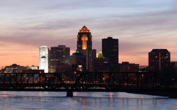 The Des Moines skyline with illuminated buildings and a bridge at sunset with colorful sky