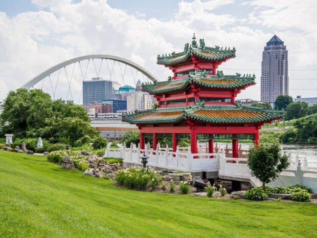 Traditional Chinese pavilion and cityscape of Des Moines in clear daylight with green lawn and bridge arch