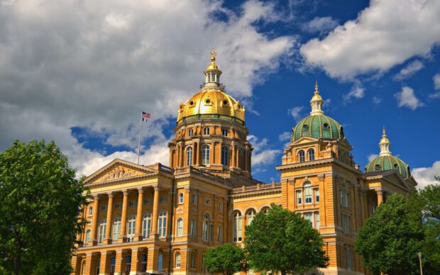 Golden dome building in Des Moines with lush green trees under a cloudy blue sky