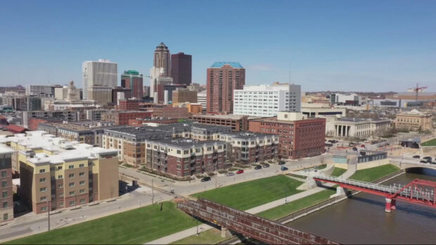 A cityscape of Des Moines with buildings and a river under a clear blue sky