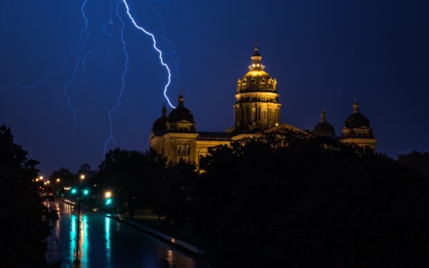 Lightning striking near the Des Moines Capitol building at night with illuminated dome and wet streets