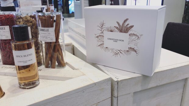 Christian Dior spice blend and cinnamon sticks displayed with branded packaging on a white wooden table