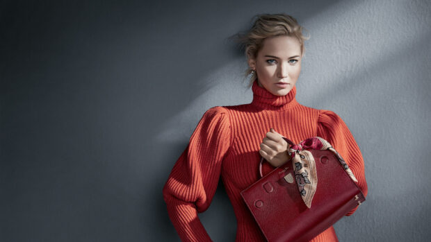 Woman with a Dior bag wearing a red sweater against a gray wall