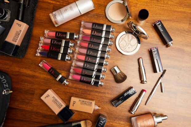 A collection of Dior cosmetic products including lipsticks and foundation on a wooden surface
