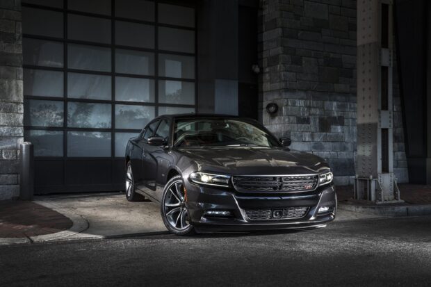 A sleek black Dodge Charger parked in front of a modern garage door with stone walls