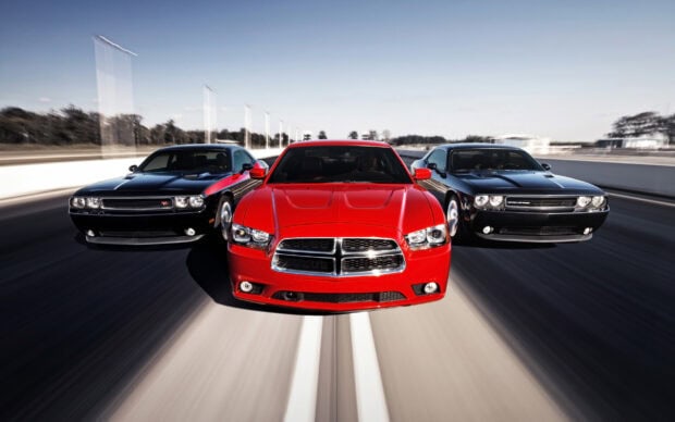 Three Dodge Charger cars driving fast on the highway with a red Charger in the center