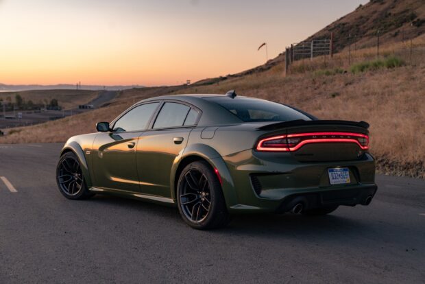 Green Dodge Charger parked on road at sunset with hills in background