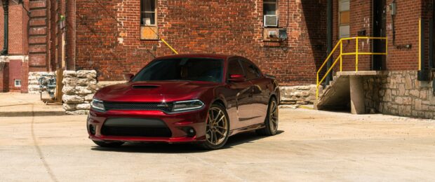 Red Dodge Charger parked in front of a brick building under bright sunlight