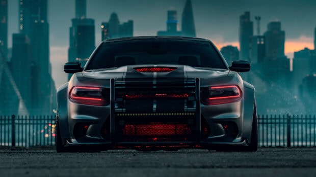 Dodge Charger parked in front of a city skyline with glowing red lights at dusk