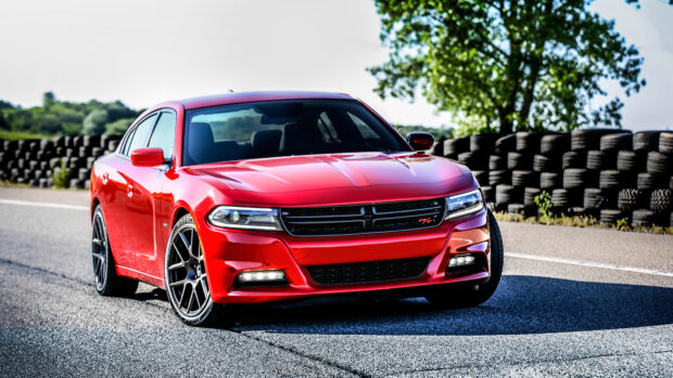 Red Dodge Charger parked on a race track with stacked tires and trees in the background