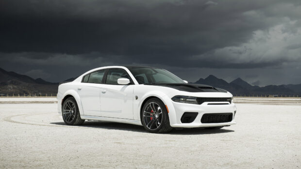 White Dodge Charger parked on a salt flat with mountains and dark cloudy sky in the background