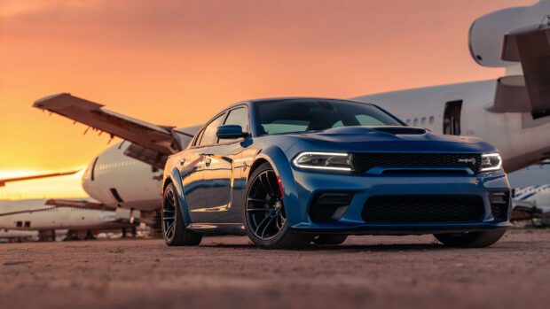 Blue Dodge Charger parked in front of airplanes during a vibrant sunset