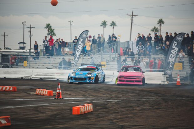 Two modified cars drifting on a track with spectators watching the drifting event