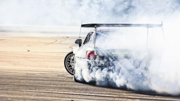 A race car drifting on the track with smoke coming from the tires
