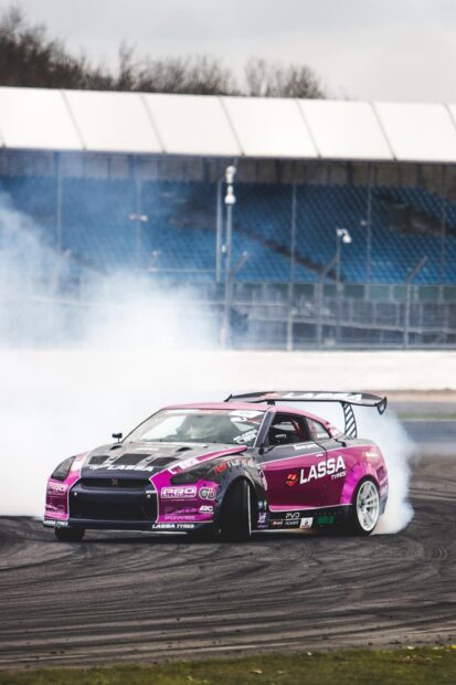 A drifting car performing a sharp turn on a race track with tire smoke around