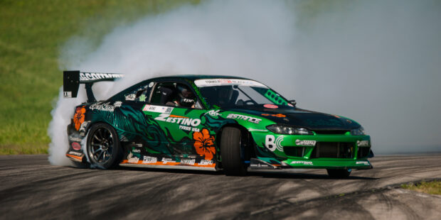 A green racing car performing drifting on a track with smoke trailing behind